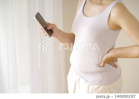 スマホを持ちお腹まわりを気にする女性 スマホを持ちお腹まわりを気にする女性 140090297
