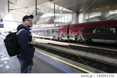 Man with a backpack waiting for a train on a platform at a modern railway station, reflecting themes of tourism and modern travel. 140091158