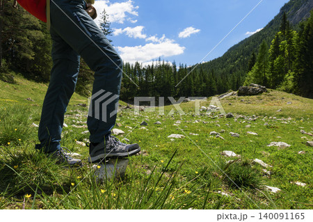 Person in hiking boots stepping on a rock in a grassy field in the Austrian Alps, highlighting active hiking in alpine terrain. 140091165
