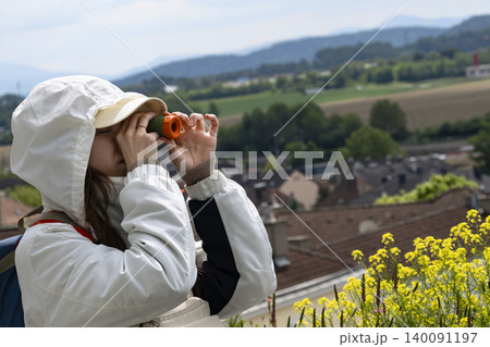 Young woman looking through a small orange telescope at a scenic landscape, showcasing a portable outdoor observation tool. Young woman looking through a small orange telescope at a scenic landscape, showcasing a portable outdoor observation tool. 140091197