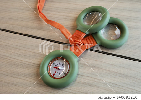 Outdoor adventure kit with a compass and magnifying glasses on a wooden table, presenting a compact outdoor exploration tool. Outdoor adventure kit with a compass and magnifying glasses on a wooden table, presenting a compact outdoor exploration tool. 140091210