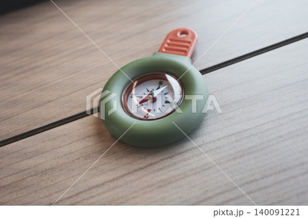 Portable green and orange compass on a wooden table, suitable for travel use and practical field tasks.  140091221