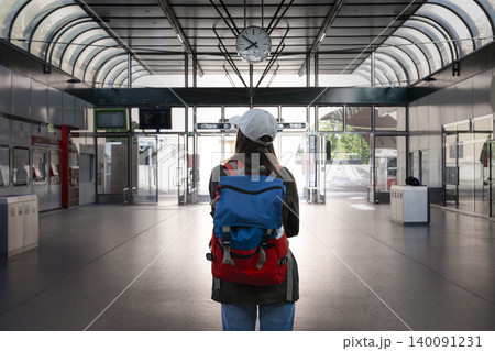 Young woman with a backpack standing at the train station beside a large round clock, symbolizing accurate timekeeping. Young woman with a backpack standing at the train station beside a large round clock, symbolizing accurate timekeeping. 140091231