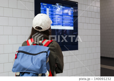 Young woman with a backpack looking at a electronic timetable at a railway station, illustrating travel planning at the station. Young woman with a backpack looking at a electronic timetable at a railway station, illustrating travel planning at the station. 140091232