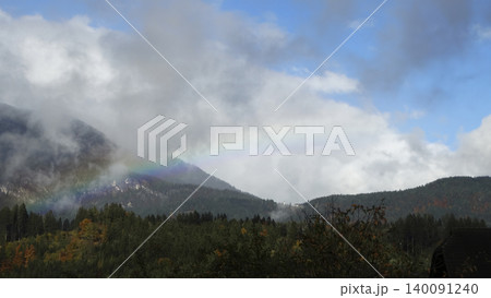 Rainbow arc over a foggy mountain landscape with clouds in the Austrian Alps, highlighting a striking natural weather phenomenon. 140091240