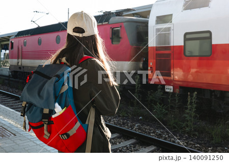Young woman with a backpack waiting for a train at a railway station, reflecting travel anticipation and boarding preparation. 140091250