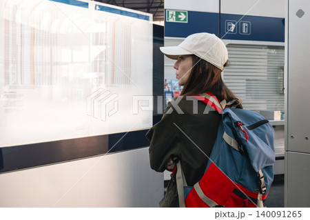 Young woman with a backpack checking the train timetable on a display with columns of information at a railway station. Young woman with a backpack checking the train timetable on a display with columns of information at a railway station. 140091265