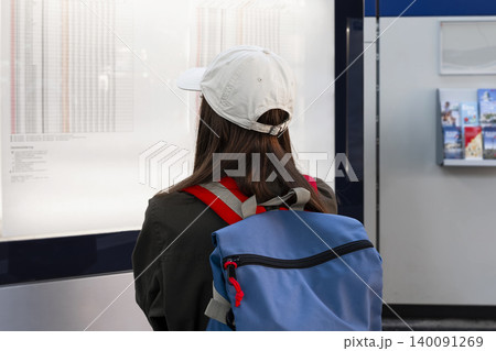 Young woman with a backpack looking at a timetable at a railway station, illustrating travel planning at the station. Young woman with a backpack looking at a timetable at a railway station, illustrating travel planning at the station. 140091269