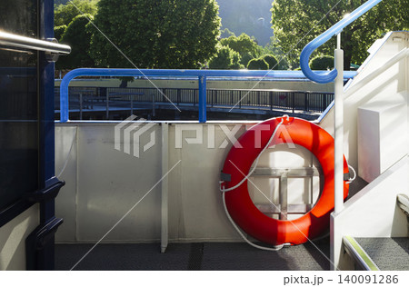 Bright orange lifebuoy on a boat deck with blue railings, representing water transport and the boating environment 140091286