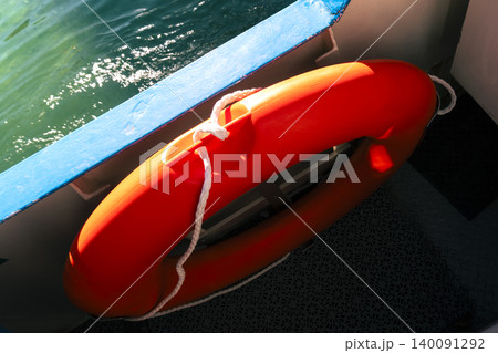 Bright orange lifebuoy on a boat deck with water in the background, illustrating maritime safety and emergency preparedness Bright orange lifebuoy on a boat deck with water in the background, illustrating maritime safety and emergency preparedness 140091292