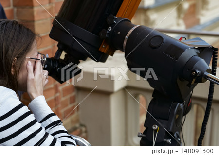 Person looking through an astronomical telescope eyepiece, illustrating hands on optical exploration while learning the sky. 140091300
