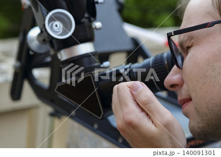 Person looking through an astronomical telescope eyepiece in a close up view, demonstrating amateur astronomy equipment in use. Person looking through an astronomical telescope eyepiece in a close up view, demonstrating amateur astronomy equipment in use. 140091301