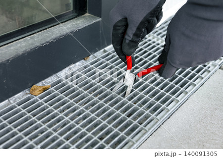 Maintenance task of a metal terrace drain grate, highlighting practical outdoor repair and routine upkeep. Maintenance task of a metal terrace drain grate, highlighting practical outdoor repair and routine upkeep. 140091305
