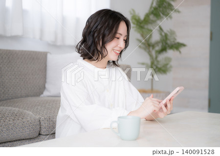 スマホを見る笑顔の女性と家でのライフスタイルイメージ snsやアプリ、買い物などを楽しむイメージ スマホを見る笑顔の女性と家でのライフスタイルイメージ snsやアプリ、買い物などを楽しむイメージ 140091528
