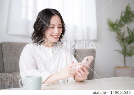 スマホを見る笑顔の女性と家でのライフスタイルイメージ snsやアプリ、買い物などを楽しむイメージ スマホを見る笑顔の女性と家でのライフスタイルイメージ snsやアプリ、買い物などを楽しむイメージ 140091529