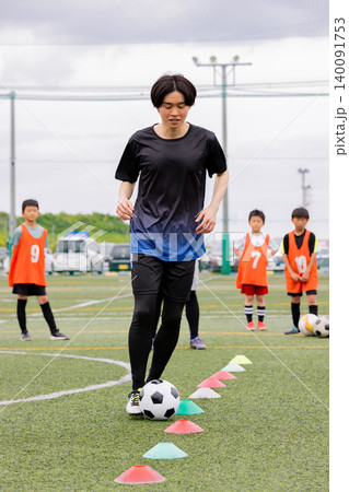フットサル練習でドリブル指導を行う男性コーチと少年たち 140091753