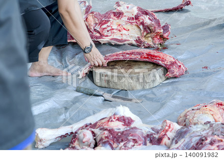 Butcher chopping raw meat with a cleaver on a wooden cutting board Butcher chopping raw meat with a cleaver on a wooden cutting board 140091982
