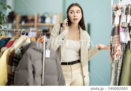 Young woman talking on mobile during shopping in clothing store Young woman talking on mobile during shopping in clothing store 140092083