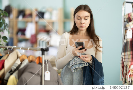 Young woman scanning QR-code on jeans pantaloons in clothing store Young woman scanning QR-code on jeans pantaloons in clothing store 140092127