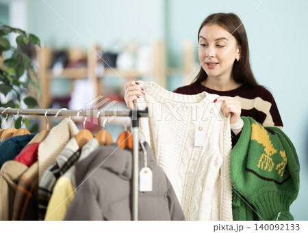 Young woman chooses sweater in clothing store Young woman chooses sweater in clothing store 140092133