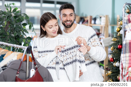 Married couple choose sweaters against background of Christmas tree in clothing store 140092201
