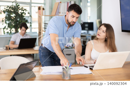 Man scolding sad female colleague working on laptop in office 140092304