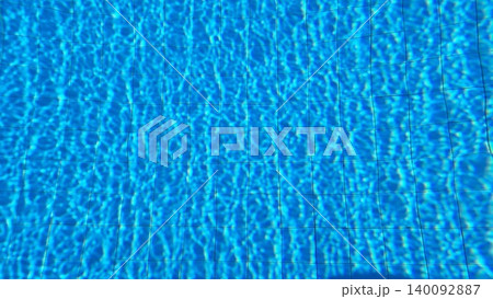 Real swimming pool water photograph featuring bright sunlight reflections, blue tiles, and dynamic ripple patterns. 140092887