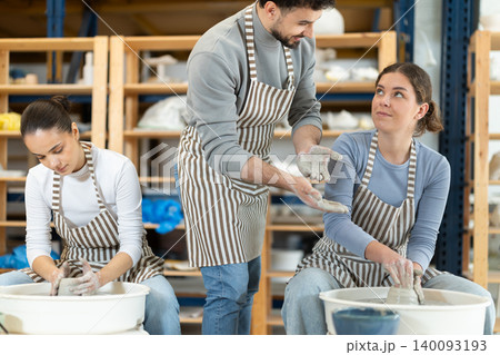 Girl craftsperson busy molding clay products using pottery wheel in lesson with male teacher Girl craftsperson busy molding clay products using pottery wheel in lesson with male teacher 140093193