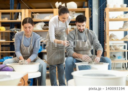 Man craftsperson busy molding clay products using pottery wheel in lesson with girl teacher Man craftsperson busy molding clay products using pottery wheel in lesson with girl teacher 140093194