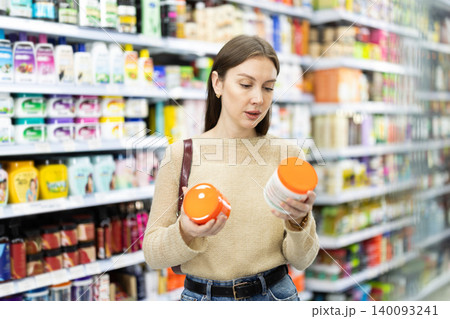 Woman spends time in store, looking for goods and select care product Woman spends time in store, looking for goods and select care product 140093241
