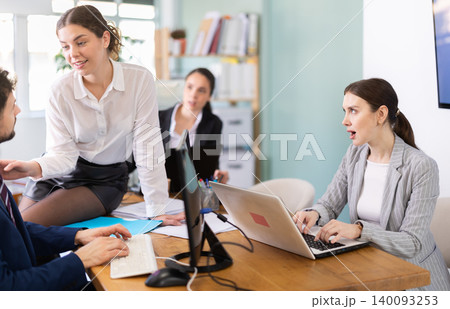 Young woman flirting with male colleague while sitting on office desk 140093253