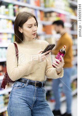Woman get acquainted with good, scan QR code, take reading label using phone camera in shop 140093344