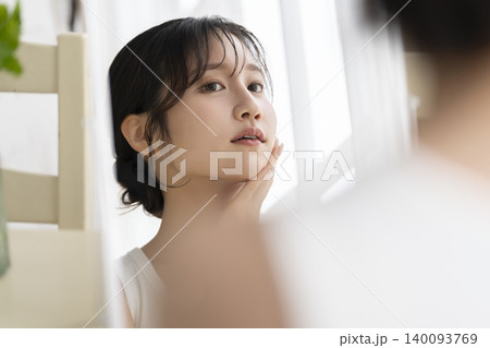 心配そうな表情で顔に手をあてて鏡を見る若い女性 140093769