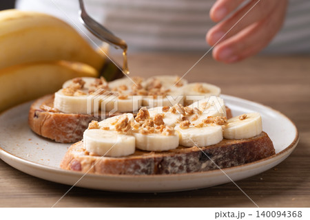 Woman's hands preparing cranberry sourdough bread with peanut butter, banana, granola and honey Woman's hands preparing cranberry sourdough bread with peanut butter, banana, granola and honey 140094368
