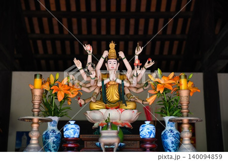 Beautiful multi armed Guanyin Bodhisattva statue sitting on lotus altar with orange lily flowers at a temple in Vietnam Beautiful multi armed Guanyin Bodhisattva statue sitting on lotus altar with orange lily flowers at a temple in Vietnam 140094859