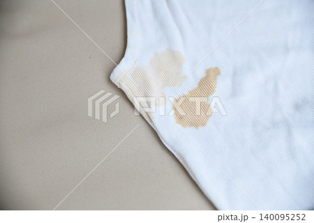 dirty yellow stains on a white rib-knit sleeveless shirt. Dirty clothes concept, sweat or food stains on fabric, laundry problem and stain removal or bleaching service background. dirty yellow stains on a white rib-knit sleeveless shirt. Dirty clothes concept, sweat or food stains on fabric, laundry problem and stain removal or bleaching service background. 140095252