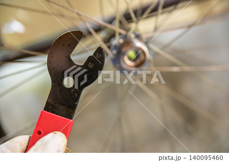 Specialty bike repair tool, cone spanner held by hand for bicycle wheel hub adjustment. a bicycle cone wrench with a blurred bike wheel hub background. Specialty bike repair tool, cone spanner held by hand for bicycle wheel hub adjustment. a bicycle cone wrench with a blurred bike wheel hub background. 140095460