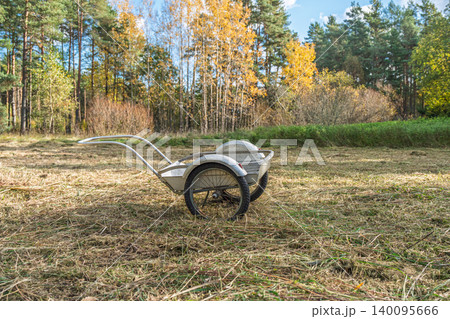 Garden cart in a field of dry grass with autumn trees in the background, outdoor scene Garden cart in a field of dry grass with autumn trees in the background, outdoor scene 140095666