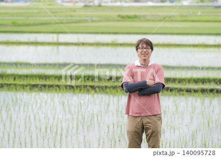 田んぼの畦道に立つ農家の男性 140095728