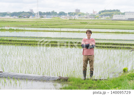 田んぼの畦道に立つ農家の男性 140095729