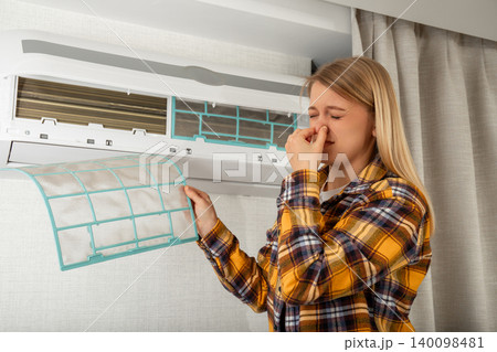 Woman examines filthy filter of air conditioner at home. Clean air and comfort concept 140098481