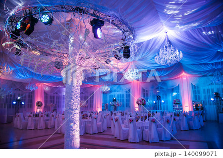 Opulent wedding reception hall with crystal chandeliers and vibrant lighting Opulent wedding reception hall with crystal chandeliers and vibrant lighting 140099071