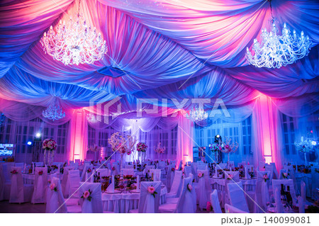 Elegant banquet hall decorated for wedding with chandeliers and pink blue lighting Elegant banquet hall decorated for wedding with chandeliers and pink blue lighting 140099081