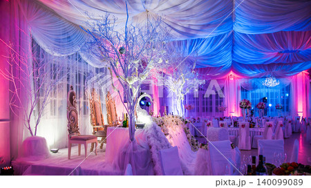Luxurious wedding reception hall with ornate table setting and vibrant pink and blue lighting 140099089