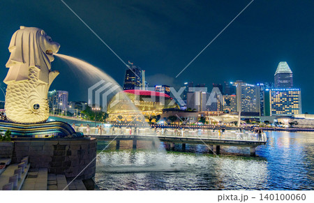 Tourist beside the Merlion statue fountain, iconic symbol of Singapore, overlooking the Marina Bay waterfront in the night Tourist beside the Merlion statue fountain, iconic symbol of Singapore, overlooking the Marina Bay waterfront in the night 140100060