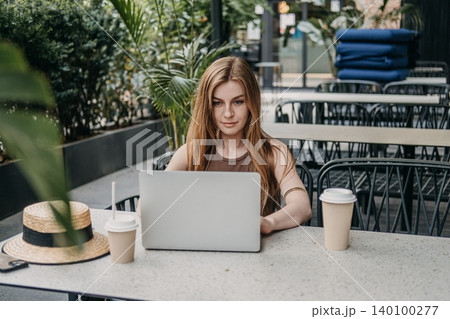 Woman types on laptop computer while sitting at outdoor cafe table. Freelance writer blogger, independent contractor job, working online terrace. Woman types on laptop computer while sitting at outdoor cafe table. Freelance writer blogger, independent contractor job, working online terrace. 140100277
