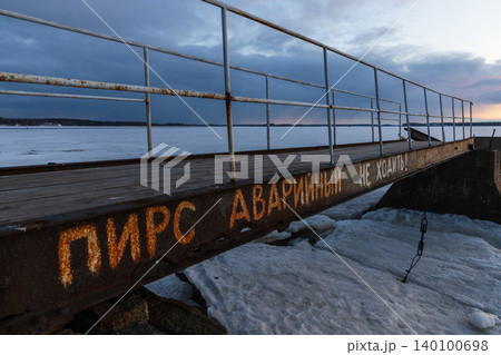 A rusty metal pier extends over a frozen lake at dusk, faded warning text 140100698