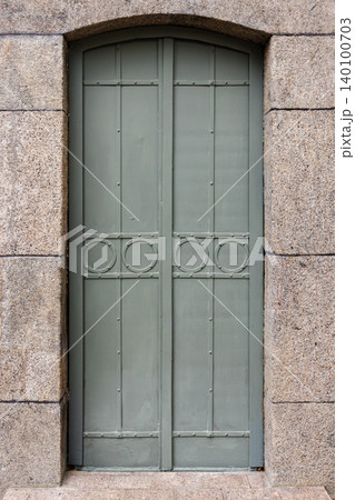 A muted green arched metal door set into a rough granite stone frame 140100703