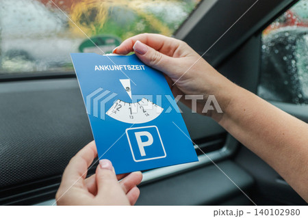 Woman holding european parking disc inside car during rainy day Woman holding european parking disc inside car during rainy day 140102980