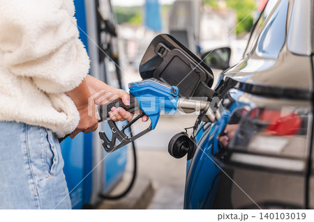 Woman refueling black automobile at gas station with blue fuel pump nozzle during modern transportation and travel activity Woman refueling black automobile at gas station with blue fuel pump nozzle during modern transportation and travel activity 140103019